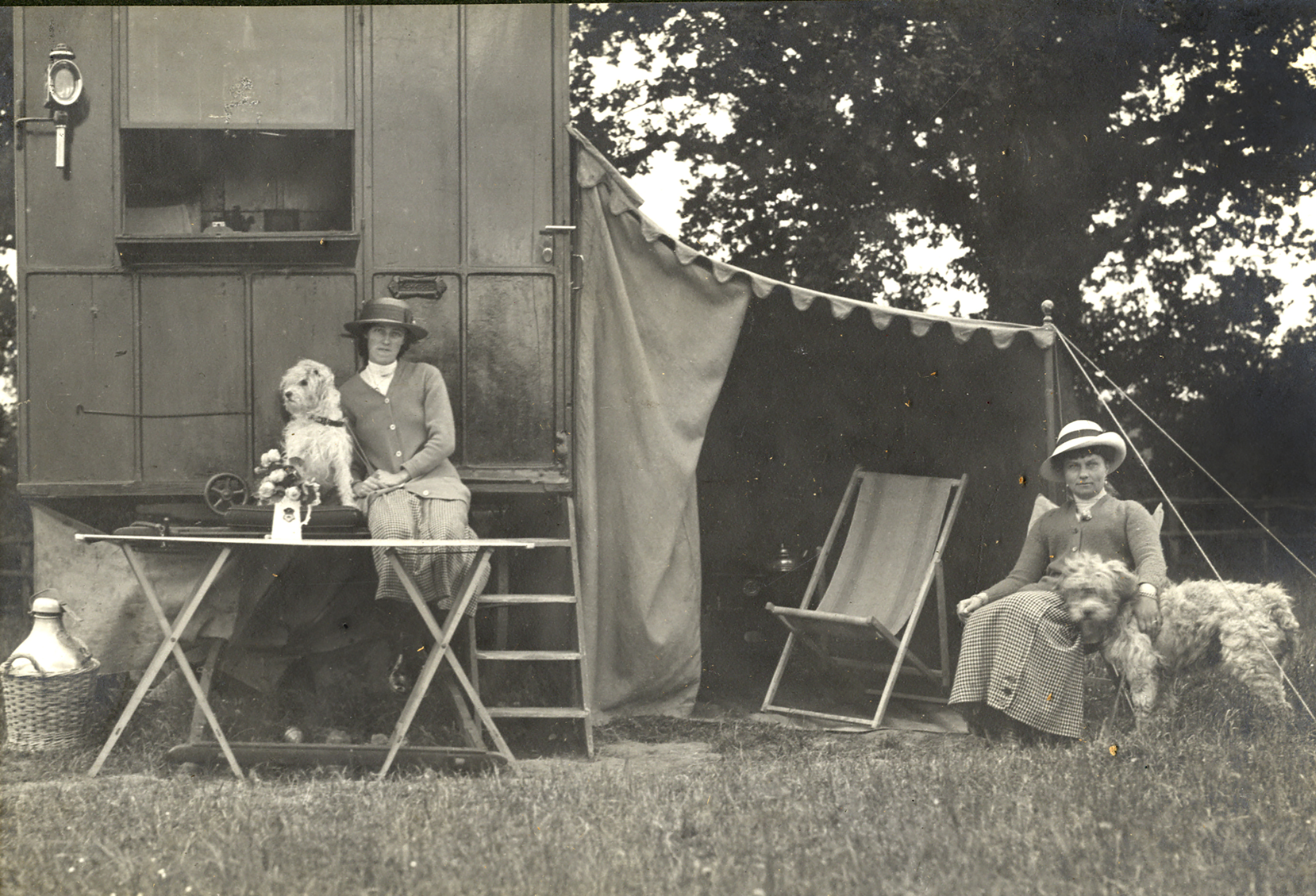 Two women Caravan Club Members seating with their dogs outside the caravan named Santa